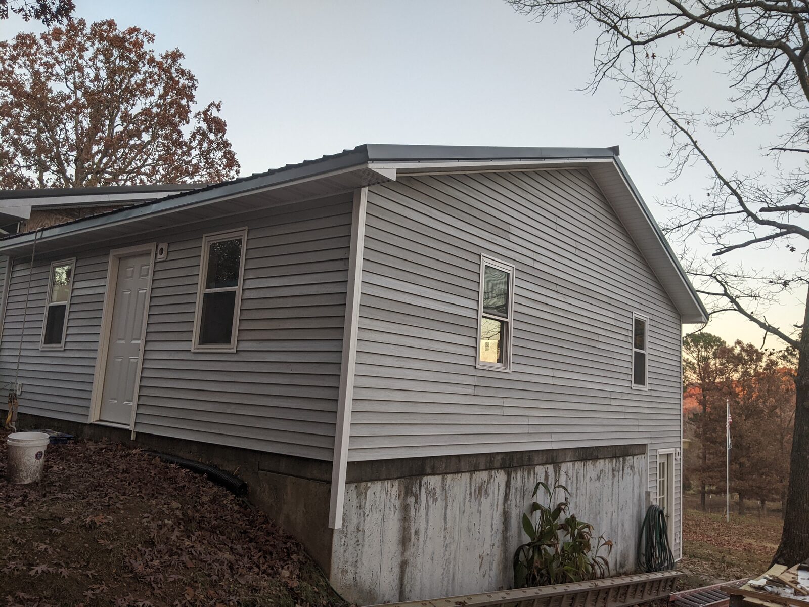 Completed single-family home with light siding and standing-seam metal roof at dusk