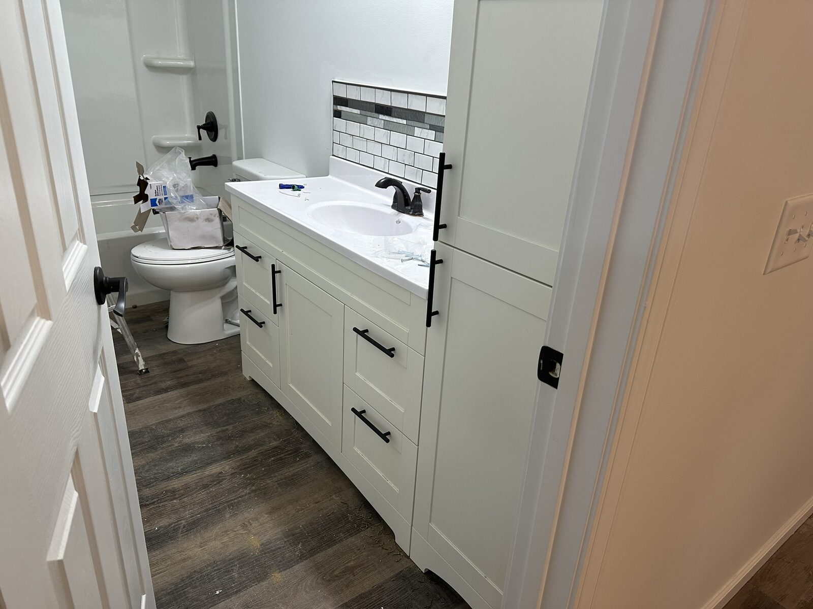 White bathroom vanity with marble counter, black faucet and accent tile backsplash