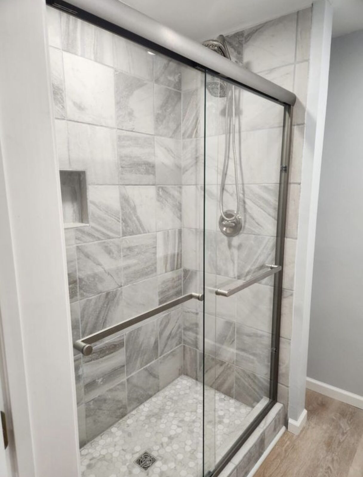 Tiled walk-in shower with gray marble tile, glass sliding door and hex mosaic floor
